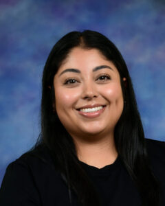 Smiling woman with long black hair, wearing a black shirt, against a blue and purple background.