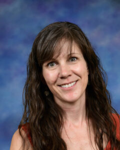 Mujer sonriente con pelo castaño largo y ondulado, vestida con un top rojo, sobre un fondo de degradado azul y morado.