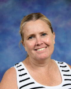 A smiling woman with blonde hair wearing a striped tank top, against a blue and purple background.