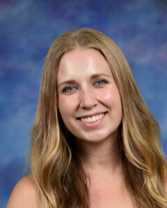 Smiling woman with long blonde hair, against a soft blue and purple background.