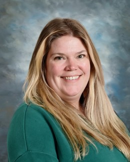 Una mujer sonriente, con el pelo largo y rubio, vestida con un top verde, posa ante un fondo azul nublado.